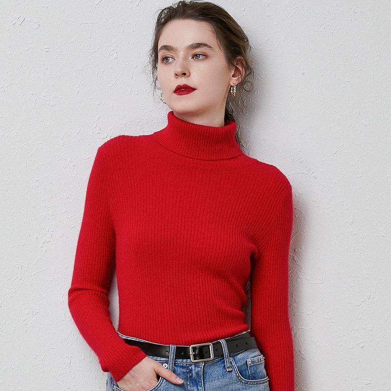 Woman wearing red ribbed turtleneck sweater and blue jeans with black belt against textured wall