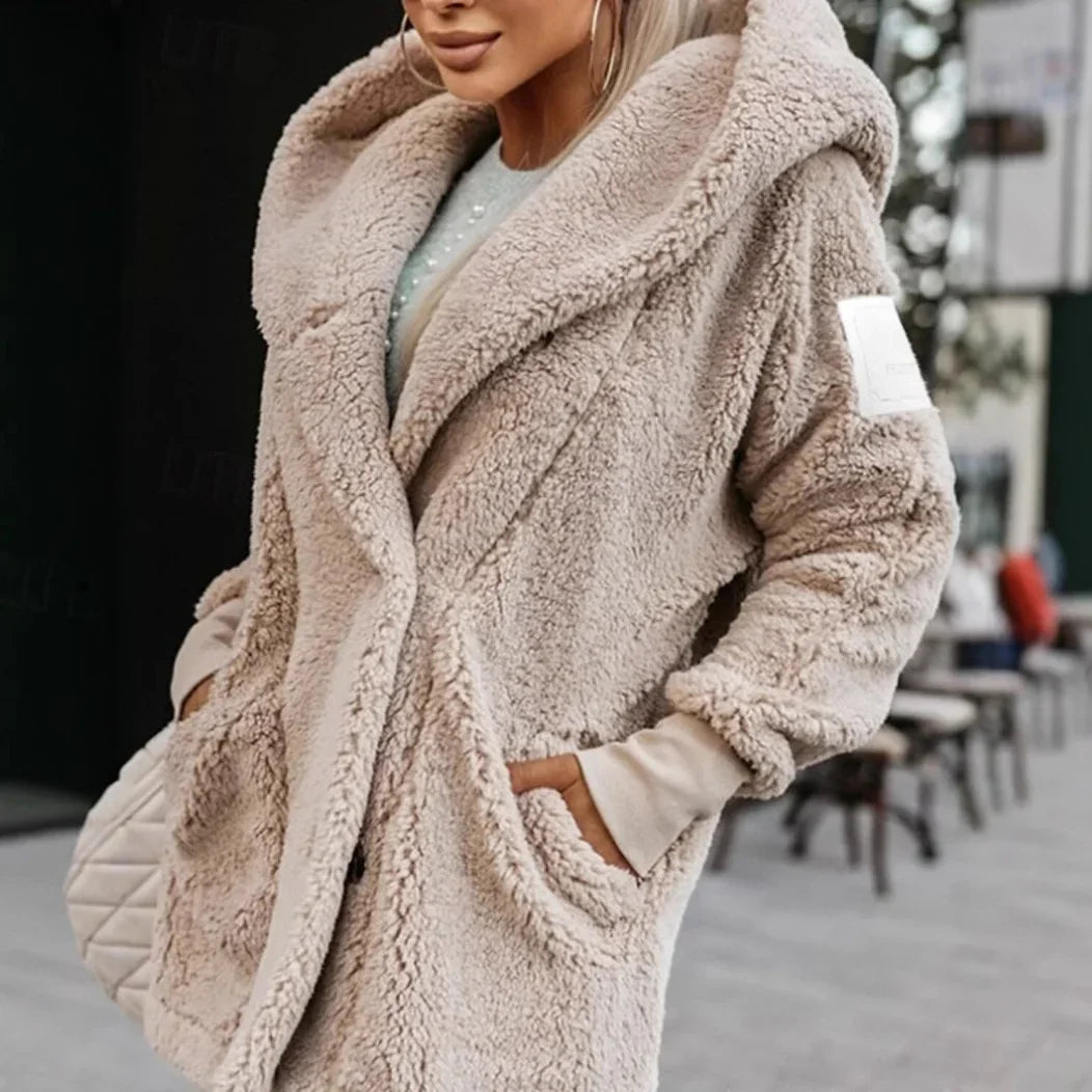 Woman wearing beige fluffy teddy coat with hood and hands in pockets on urban street
