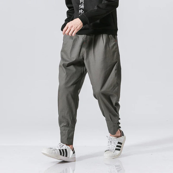 Man wearing loose grey jogger pants and white sneakers with black stripes on white background