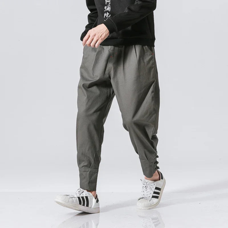Man wearing gray tapered pants with ankle button details and white Adidas sneakers
