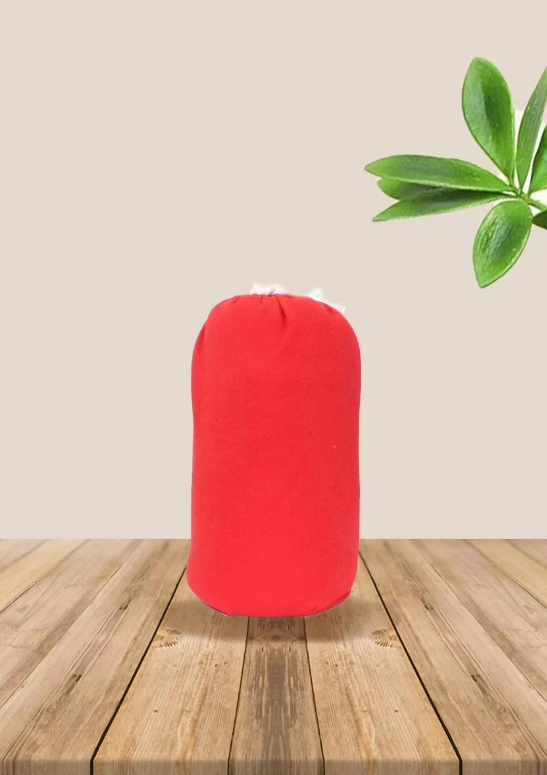 Red cylindrical pillow with fluffy white filling on wooden surface with green leaves in background