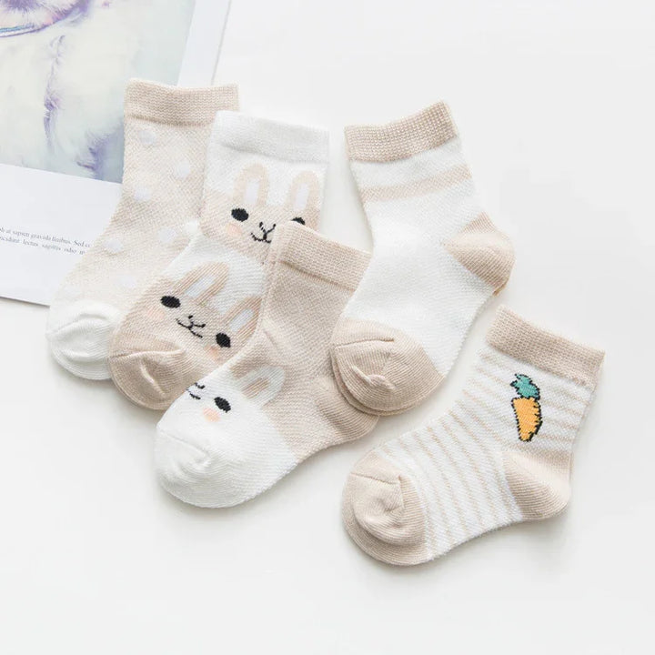 Five pairs of beige and white baby socks with bunny faces, polka dots, stripes, and carrot design