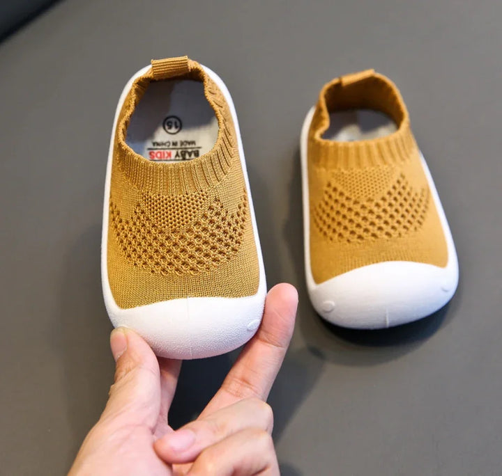 Pair of mustard yellow baby shoes with white toes on gray surface, one held by hand