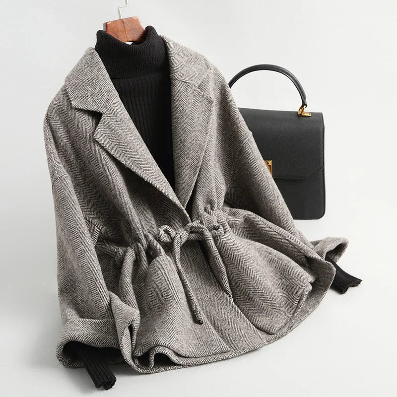 Gray herringbone belted coat over black turtleneck sweater with black leather handbag