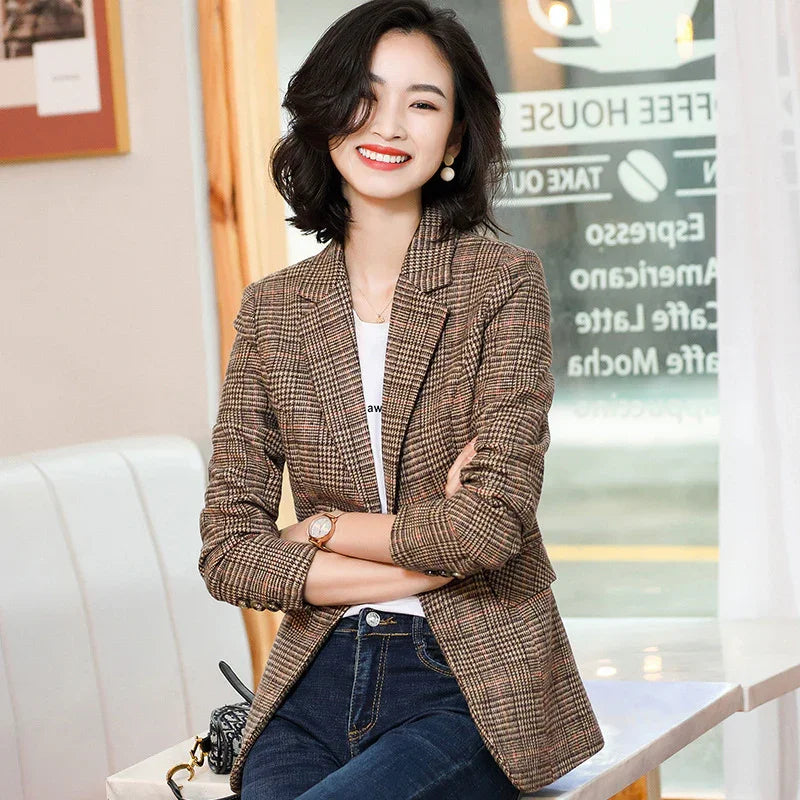 Smiling woman in a brown plaid blazer and jeans sitting in a modern cafe with coffee menu in background