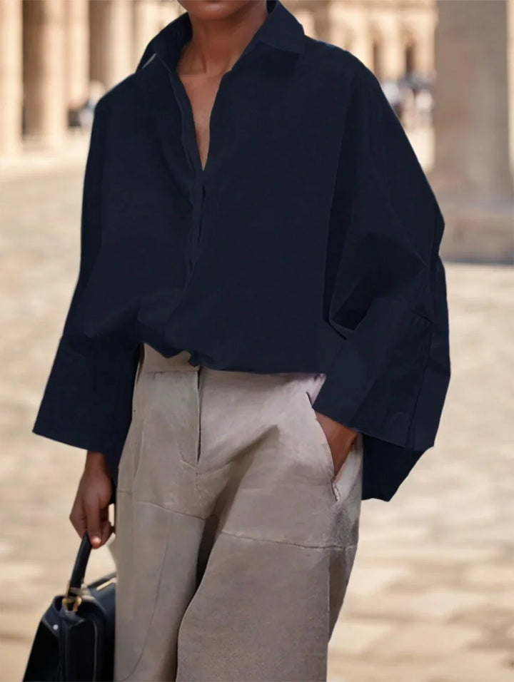 Person wearing oversized black shirt and beige trousers, holding black handbag in outdoor corridor