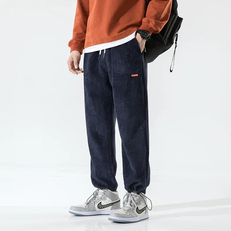 Person wearing navy blue corduroy pants with elastic cuffs, white and gray sneakers, and an orange sweatshirt