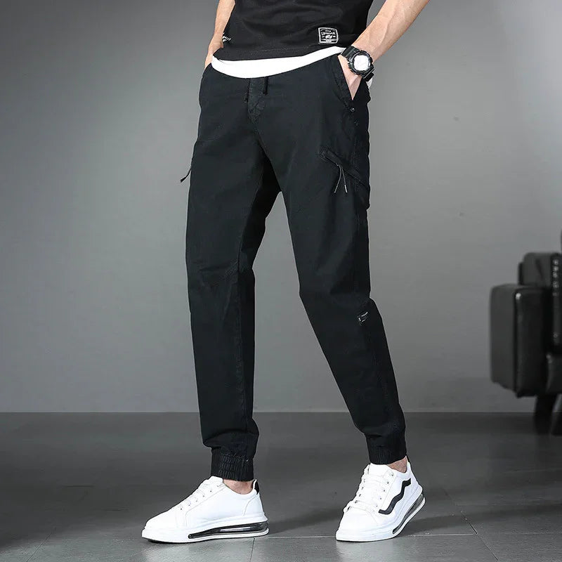 Man wearing black cargo jogger pants and white sneakers standing indoors on gray floor
