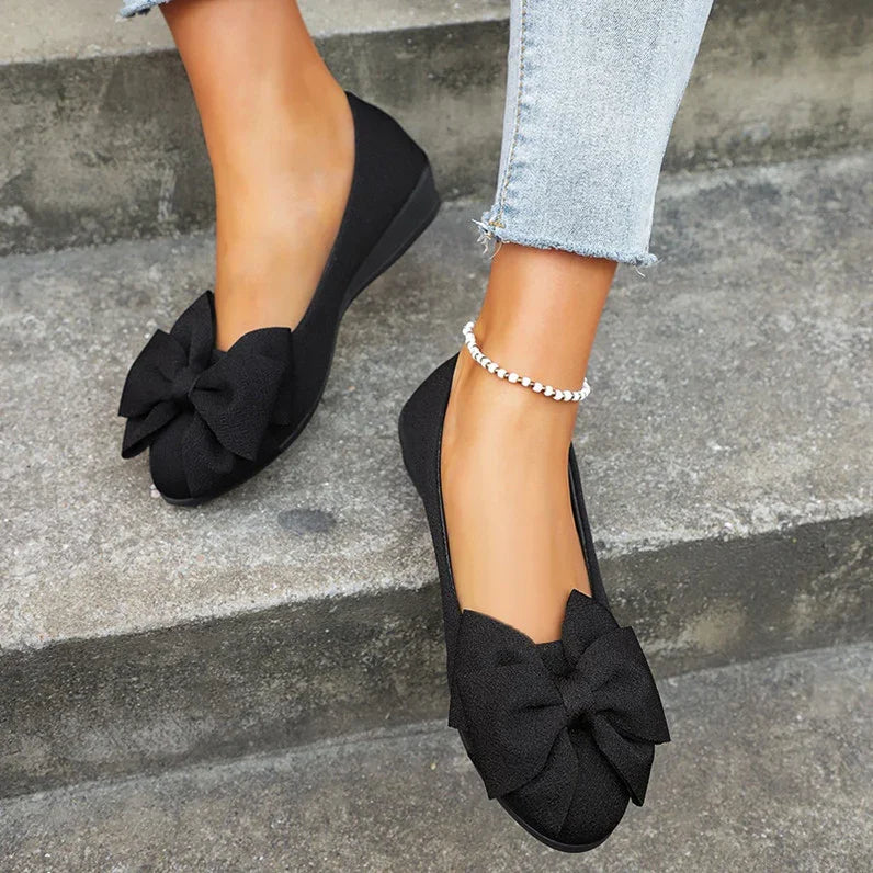 Woman wearing black bow flats and light blue jeans sitting on concrete steps, ankle bracelet visible