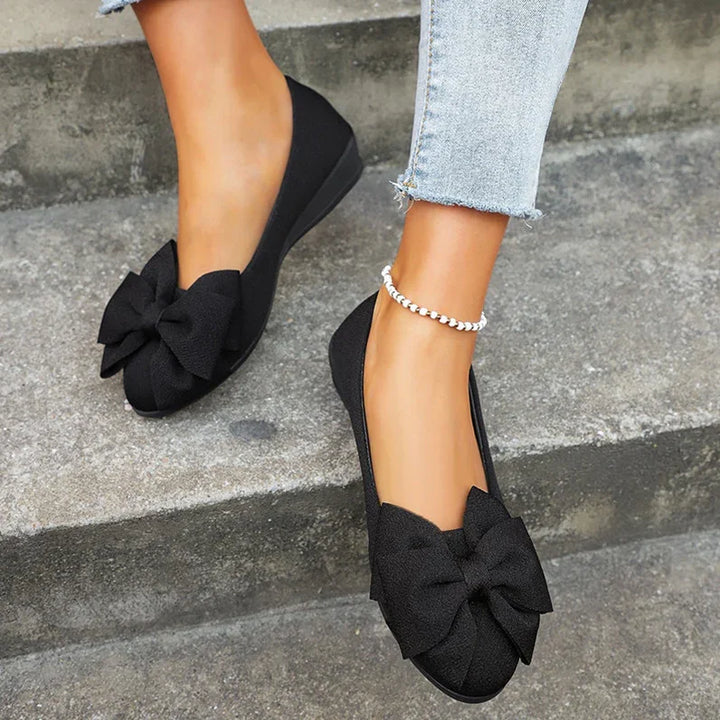Woman wearing black bow flats and light blue jeans sitting on concrete steps, ankle bracelet visible