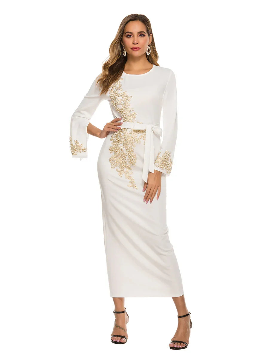 Woman wearing white long-sleeve midi dress with gold floral embroidery and belt, black heels