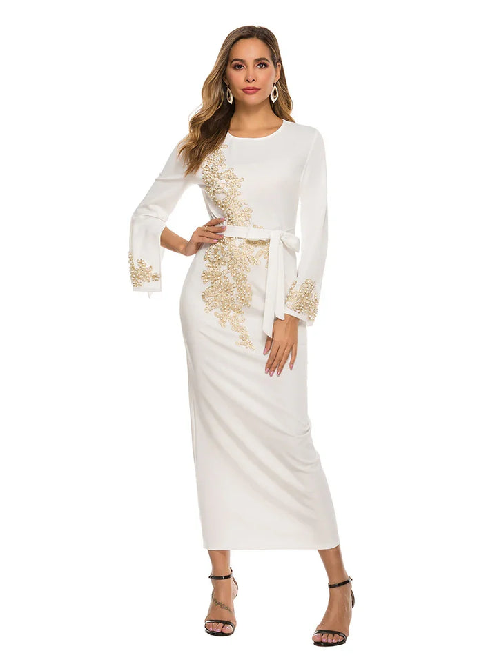 Woman wearing white long-sleeve midi dress with gold floral embroidery and belt, black heels