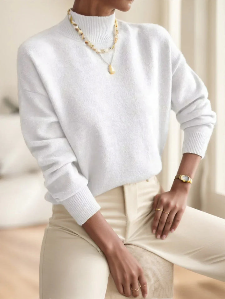 Woman wearing white cozy sweater with cream pants, gold watch, rings, and layered necklaces