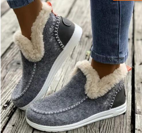 Gray fleece-lined slip-on winter shoes with white soles worn with blue jeans on wooden deck