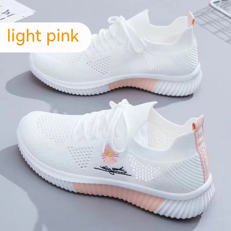 White knitted sneakers with light pink soles and decorative flower detail, on gray surface