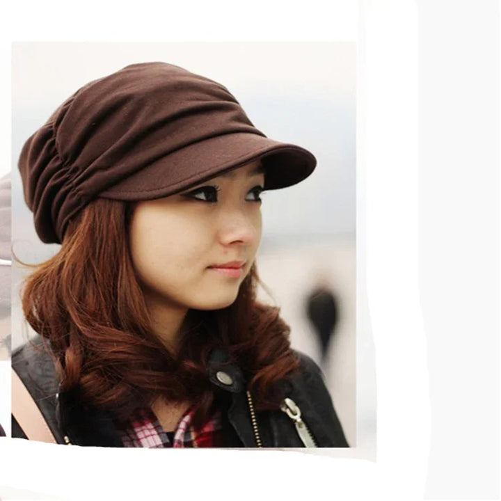 Young woman with brown curly hair wearing a brown cap and black jacket outdoors