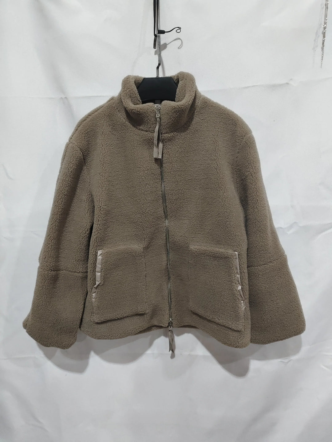 Beige zip-up fleece jacket with high collar and front pockets hanging on black hanger