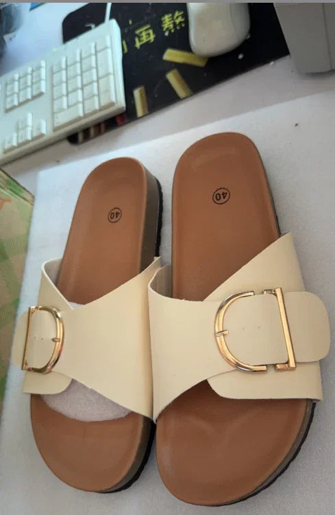 Pair of beige slide sandals with gold buckle on brown footbed, size 40, placed near computer keyboard