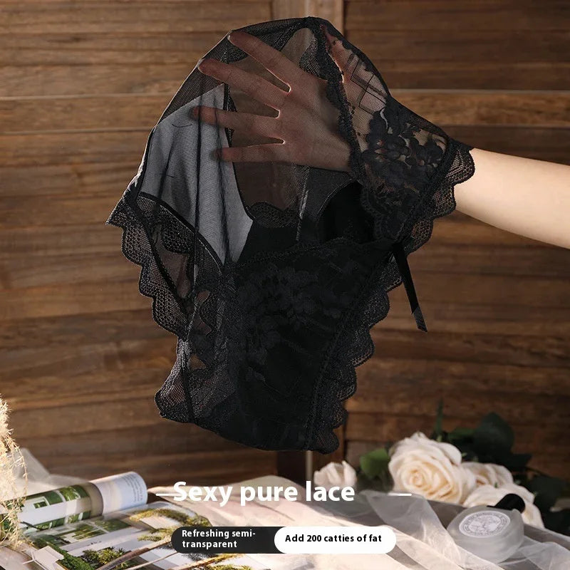Hand holding black sheer lace lingerie with floral patterns against wooden background