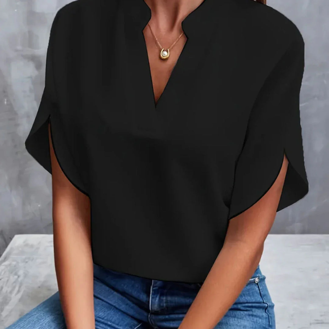 Woman wearing black v-neck slit sleeve top paired with blue jeans and gold pendant necklace
