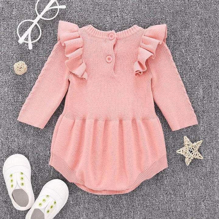 pink knitted baby dress with ruffles on shoulders, white baby shoes, white glasses on grey fabric background