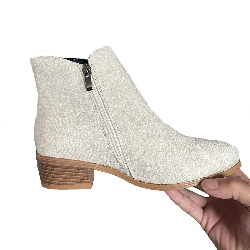 Hand holding beige suede ankle boot with side zipper and wooden low heel