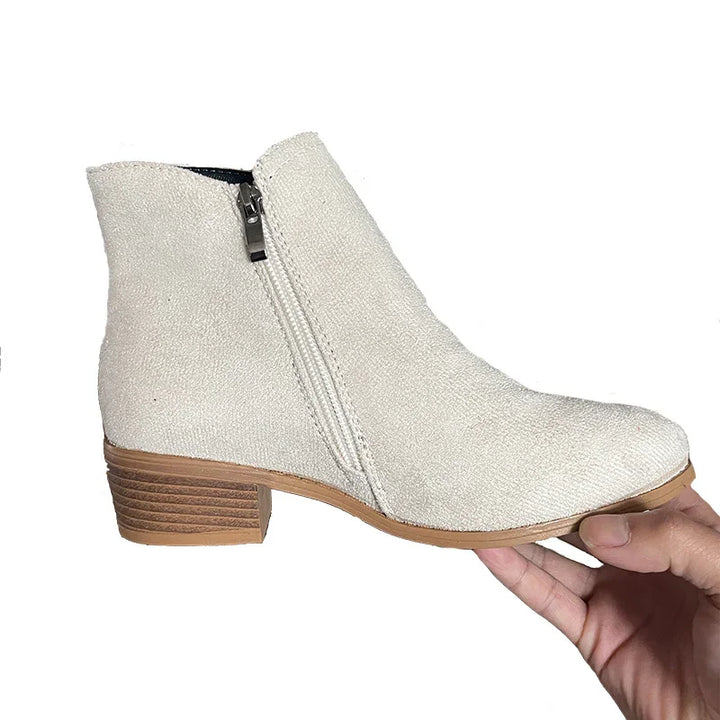 Hand holding beige suede ankle boot with side zipper and wooden low heel