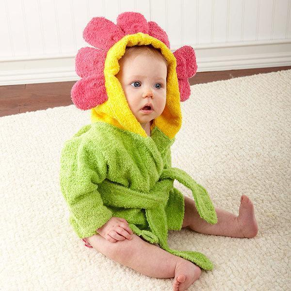 Baby sitting on carpet wearing green bathrobe with pink flower hood in bright indoor setting