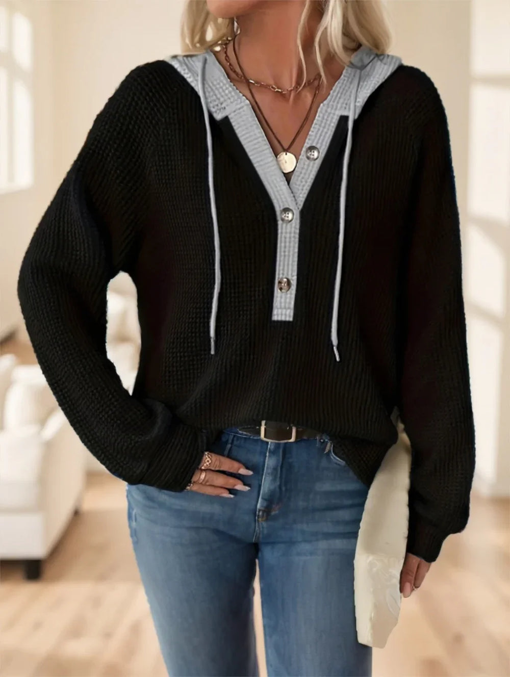Woman wearing black knit hoodie with gray button placket and light blue jeans in bright living room