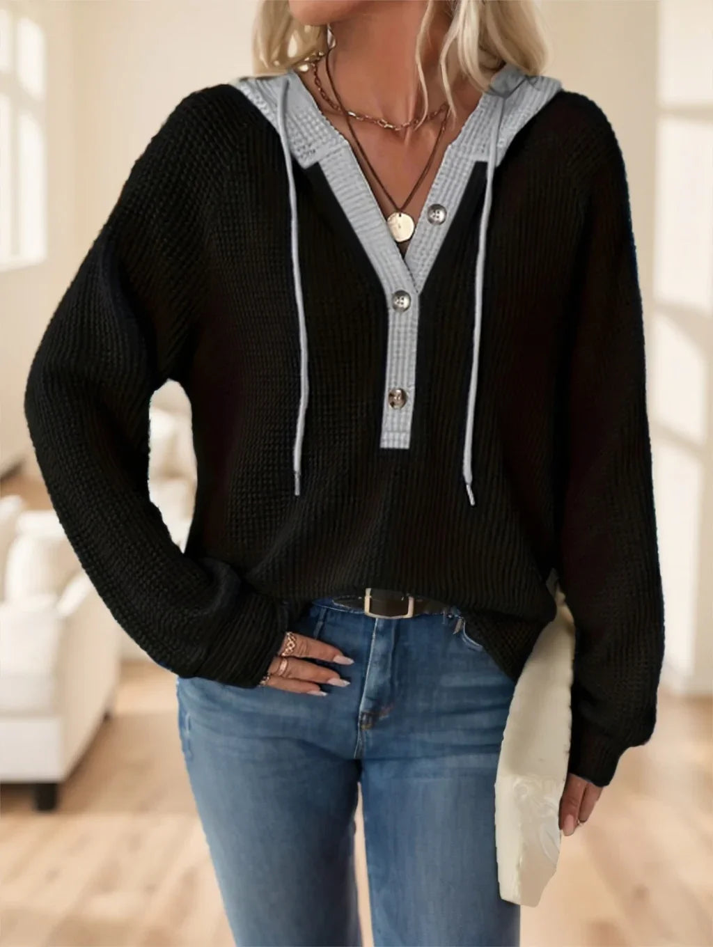 Woman wearing black knit hoodie with gray button placket and light blue jeans in bright living room