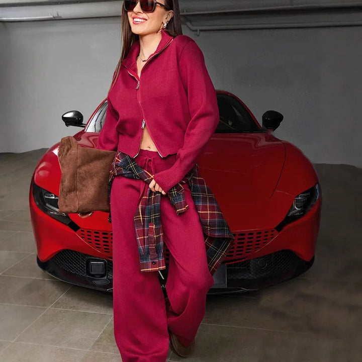 Smiling woman in red athleisure with sunglasses stands in front of a red sports car in garage