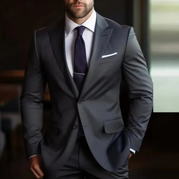 Man in tailored dark gray suit with white shirt, navy tie, and pocket square in modern setting