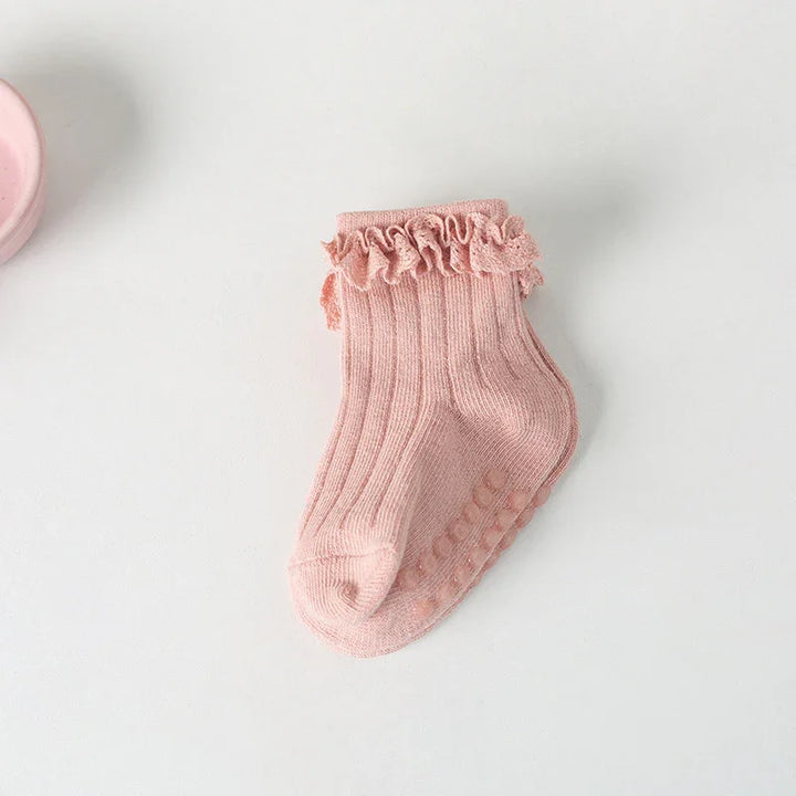 Single pink baby sock with ruffled cuff and grip dots on sole on white surface