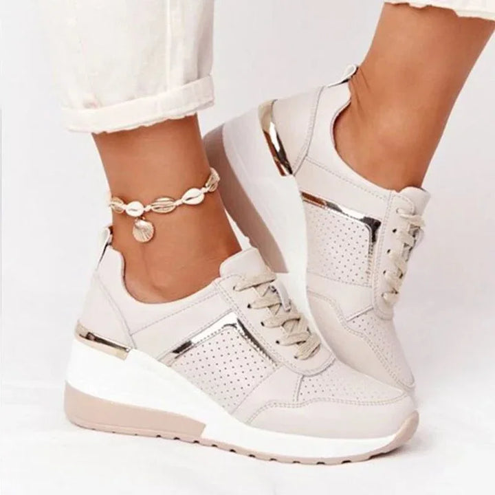 Beige platform wedge sneakers with metallic accents and perforated design worn with white pants and shell anklet