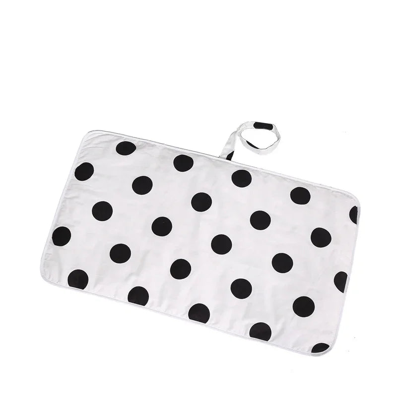White rectangular changing mat with large black polka dots and attached strap with velcro