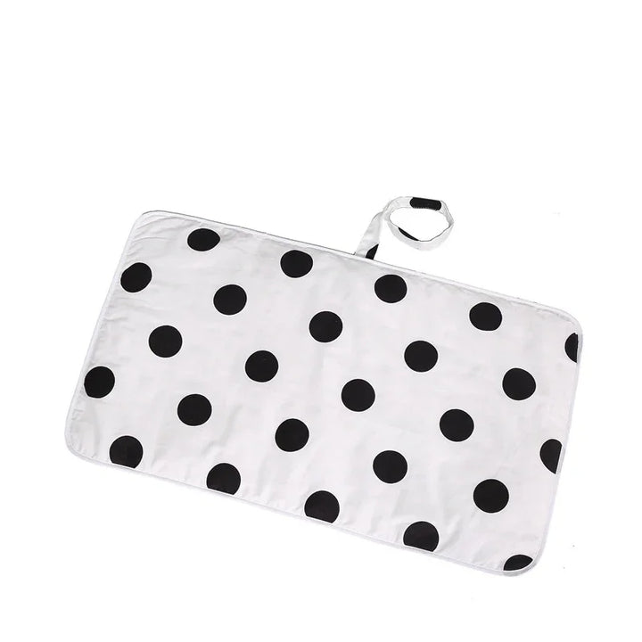 White rectangular changing mat with large black polka dots and attached strap with velcro
