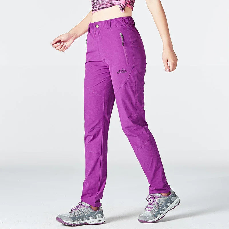 Woman wearing purple outdoor hiking pants and gray athletic shoes against white background