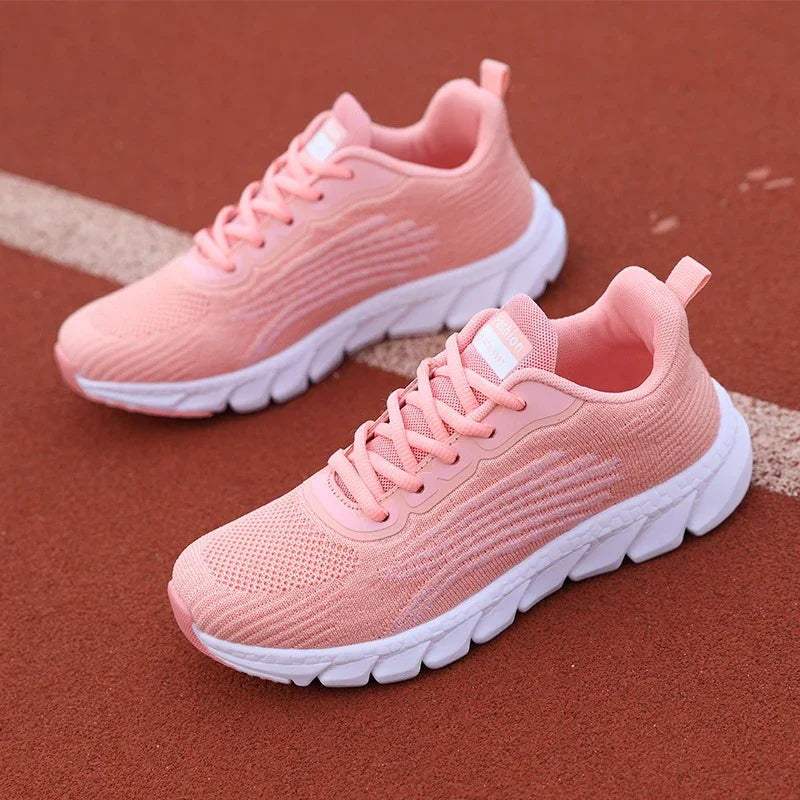 Pair of pink knit running shoes with white chunky soles on a red track surface