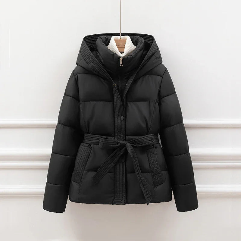 Black padded winter jacket with hood and belt hanging on wooden hanger against white wall