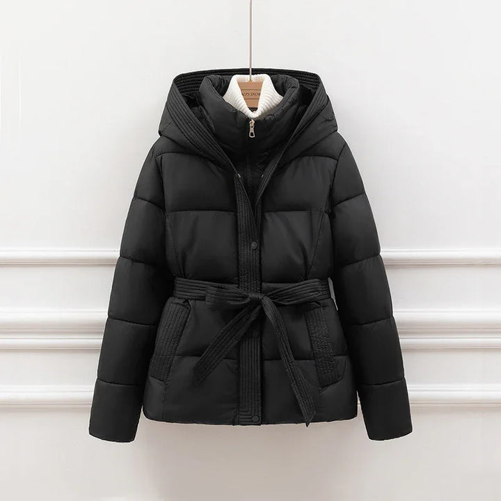 Black padded winter jacket with hood and belt hanging on wooden hanger against white wall