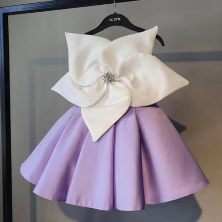 Purple A-line dress with oversized white flower embellishment on bodice, hanging on black SC Stil hanger