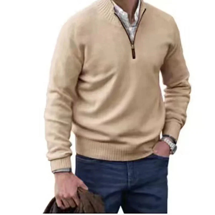 Man wearing beige quarter-zip sweater over white shirt and blue jeans holding brown jacket