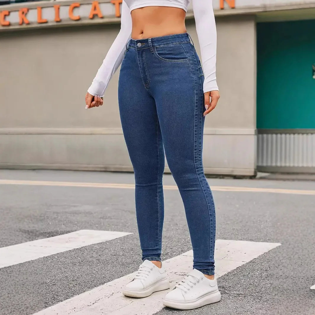 Woman wearing high-waisted blue skinny jeans and white sneakers standing on city street