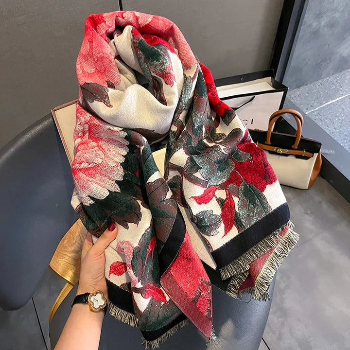 Hand holding a floral red and green scarf with black fringe over a chair, luxury handbags in the background