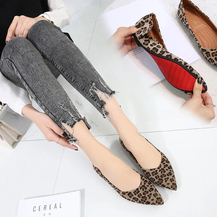 Woman wearing leopard print pointed flats with red soles and distressed grey skinny jeans on white tile floor