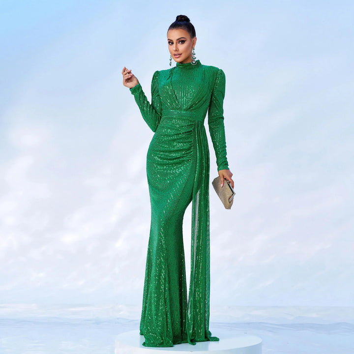 Woman wearing a long green sequin evening gown with long sleeves, holding a silver clutch