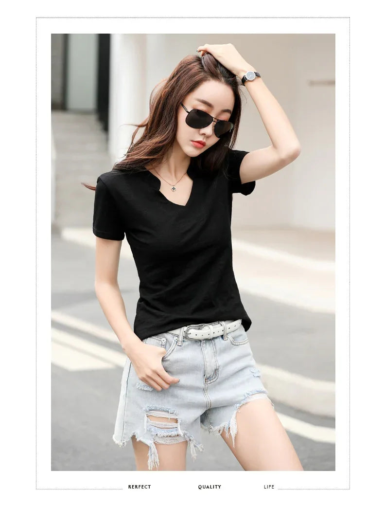 Woman wearing black v-neck t-shirt, ripped light denim shorts, sunglasses, and wristwatch outdoors