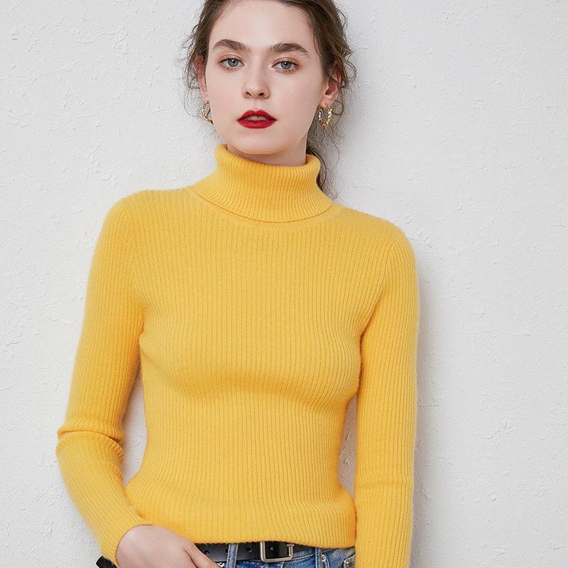 Woman wearing a yellow ribbed turtleneck sweater with gold hoop earrings against a white textured wall