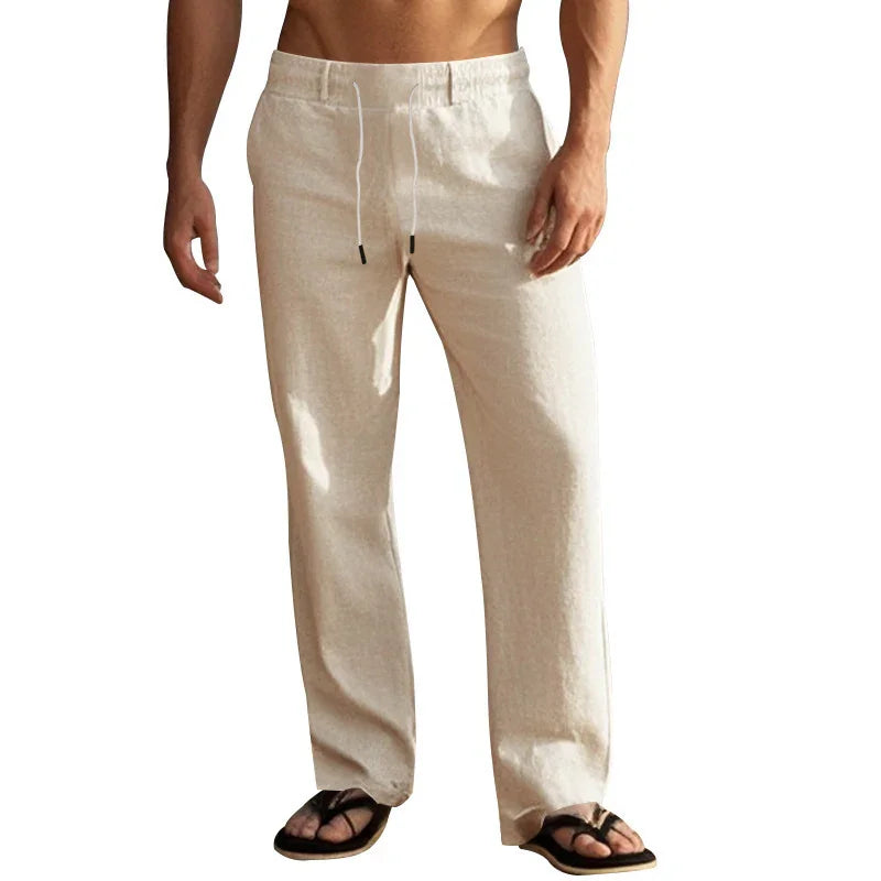 Man wearing beige linen drawstring pants and black flip-flops standing isolated on white