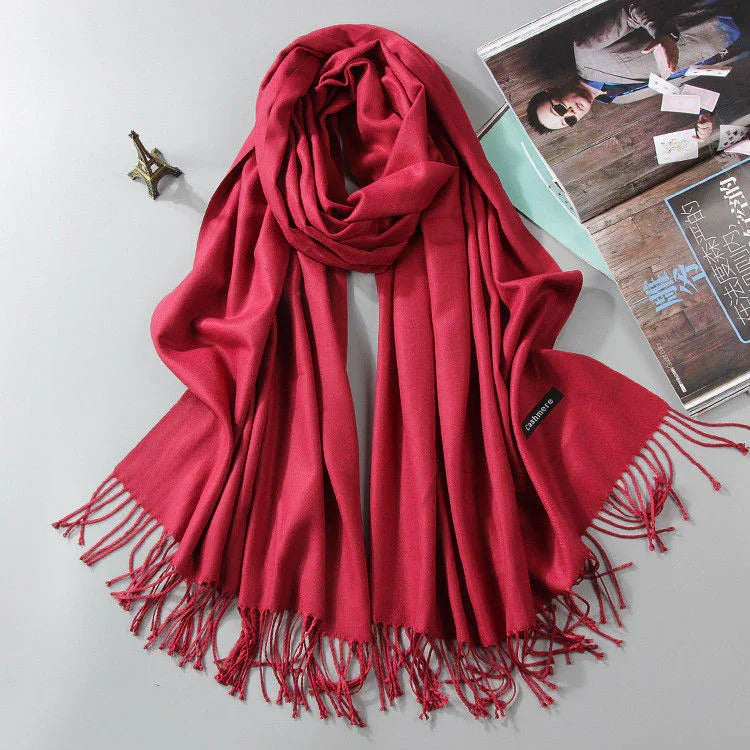 Soft red cashmere scarf with fringed edges displayed beside a small Eiffel Tower model and a magazine